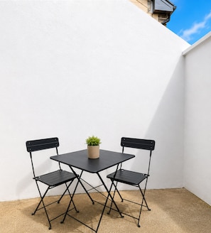 A small outdoor patio with a table and two chairs, a potted plant, and a white wall. - Kilkee Townhouse (Kilkee)