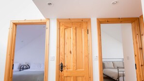 A room with a wooden door, a bed with a metal frame, and a small table. - Kilkee Townhouse (Kilkee)