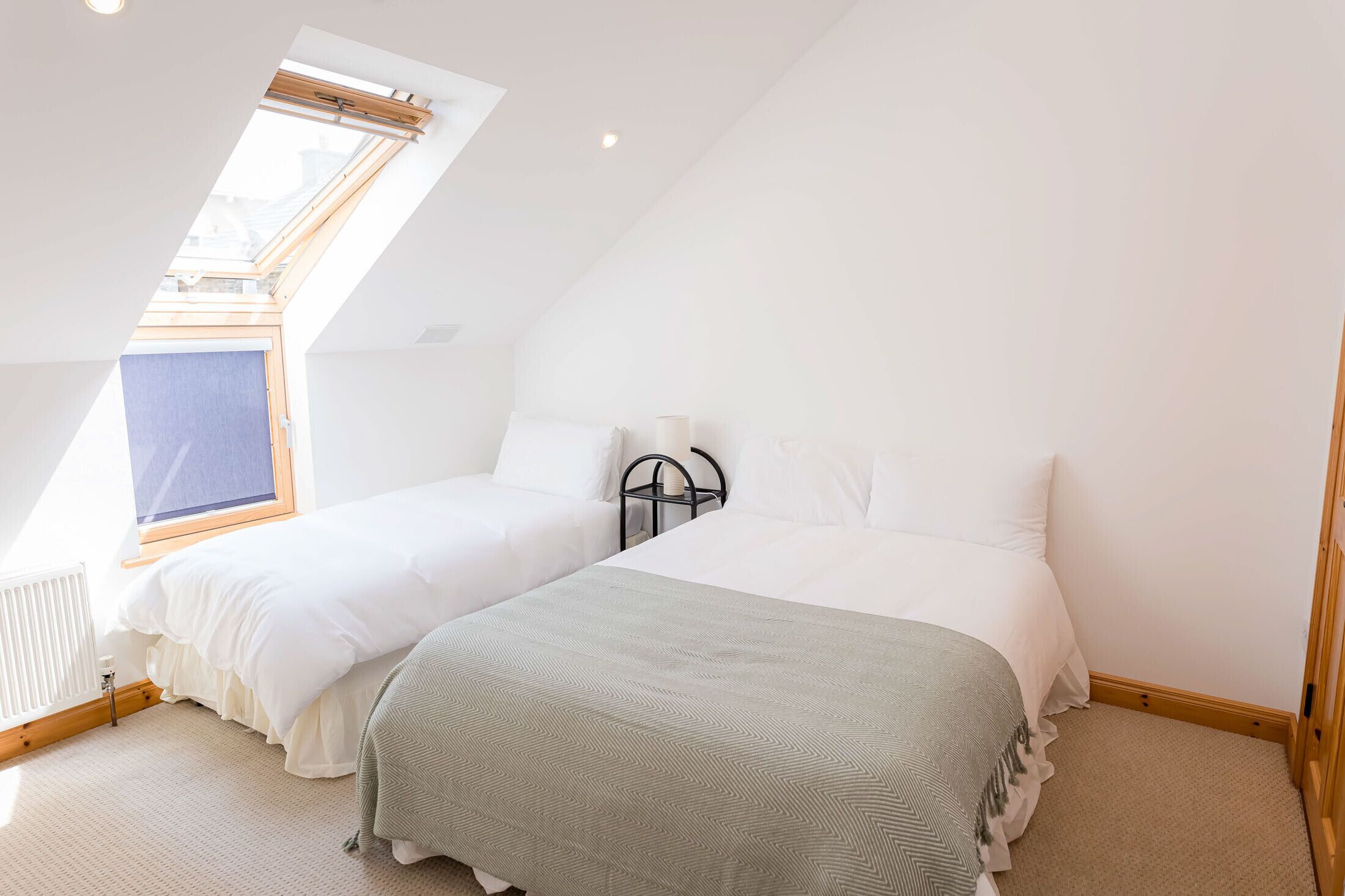 A bedroom with two beds, a skylight, and a radiator.
