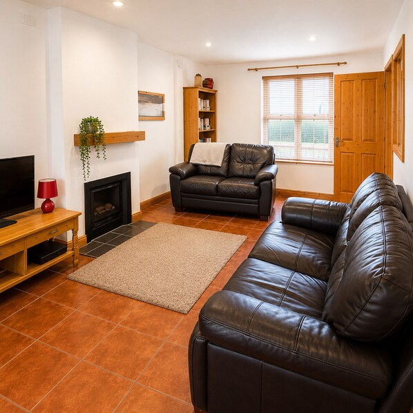 A living room with a fireplace, leather sofa, wooden bookshelf, and a television.