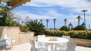 Un patio con sillas y una mesa blancos, palmeras y vistas al mar.