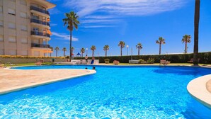 Piscina con agua cristalina azul, rodeada de palmeras y un edificio con balcones.