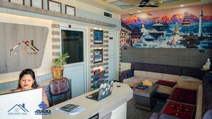 A hotel reception area with a reception desk, a sofa, and a mural of mountains. - Hotel Happy Home (Siddharthanagar)