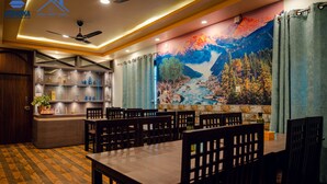 A restaurant with a mural of a mountain landscape, wooden tables and chairs, and a bar area with shelves of bottles. - Hotel Happy Home (Siddharthanagar)