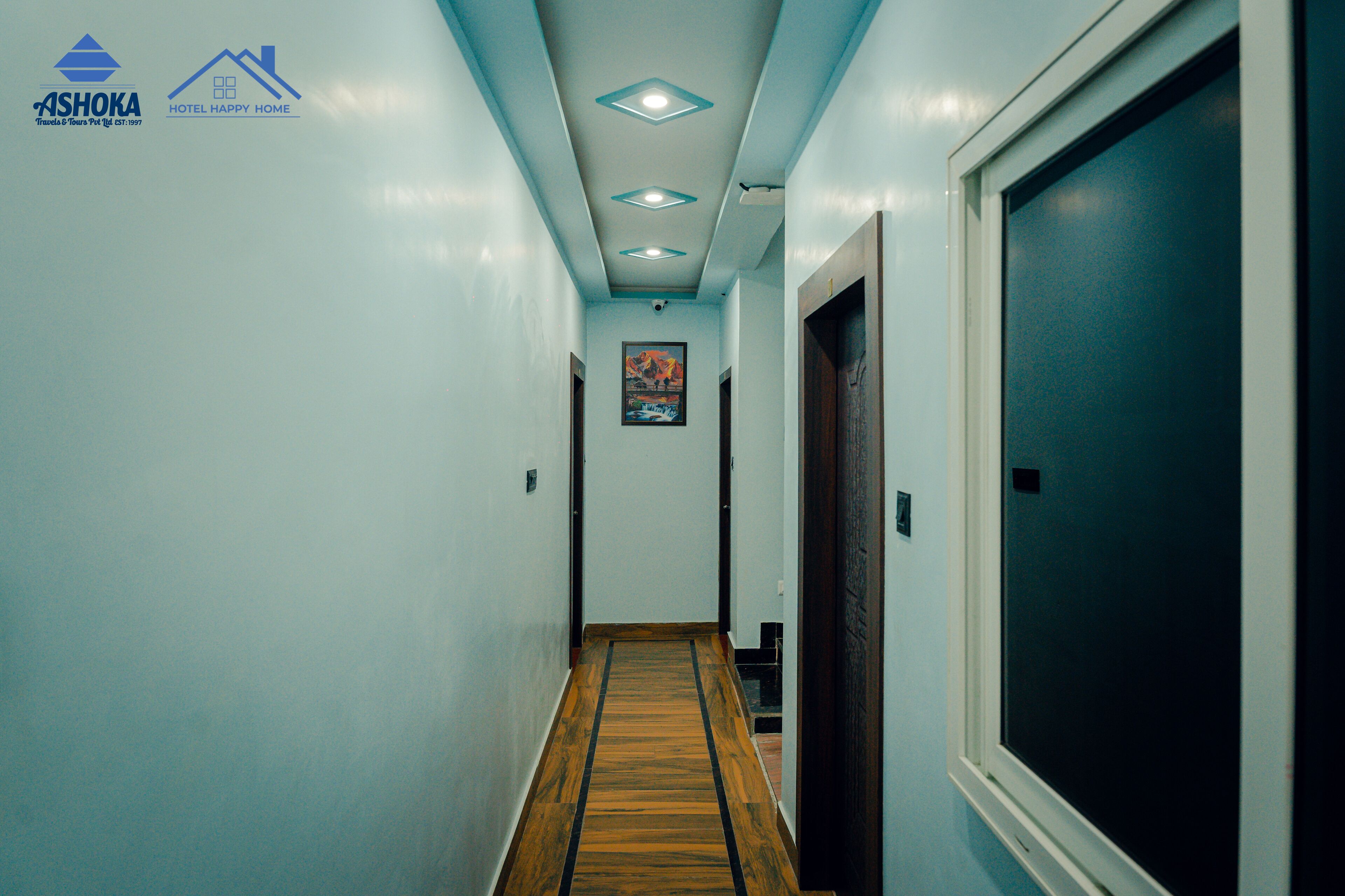 A hotel hallway with a wooden floor, light blue walls, and a ceiling with recessed lighting.
