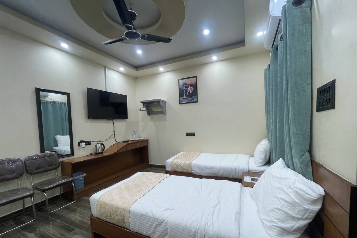 A hotel room with two beds, a desk, a chair, a television, and a ceiling fan.