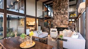 Un espacio habitable amplio con chimenea de piedra, una mesa de comedor con un florero y una escalera que sube a un nivel superior.