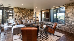 Una sala de estar moderna con una pared de acento de piedra, muebles de cuero y una puerta de vidrio que da al exterior.
