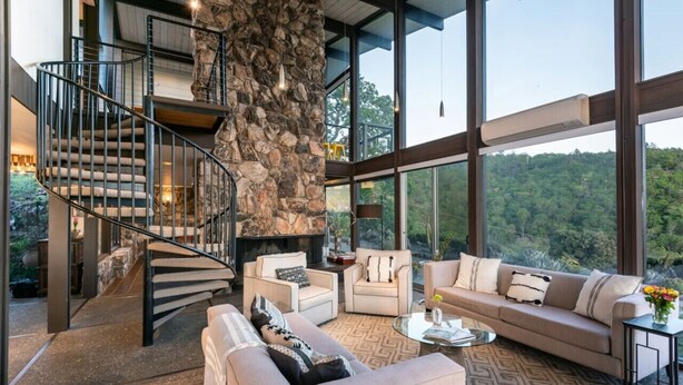 Un interior moderno con una pared de acento de piedra, una escalera de caracol y un gran ventanal con vistas al exterior.