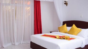 Ein Hotelzimmer mit einem Bett, weißen Vorhängen, einem roten Vorhang und einer Wandleuchte.