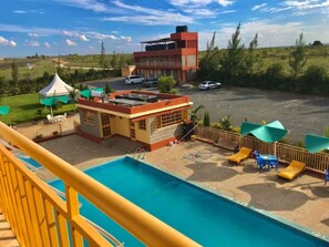 A pool area with a clear view of the surrounding landscape, including a building with a red roof and a white tent. - The Lukenya Resort (Athi River)