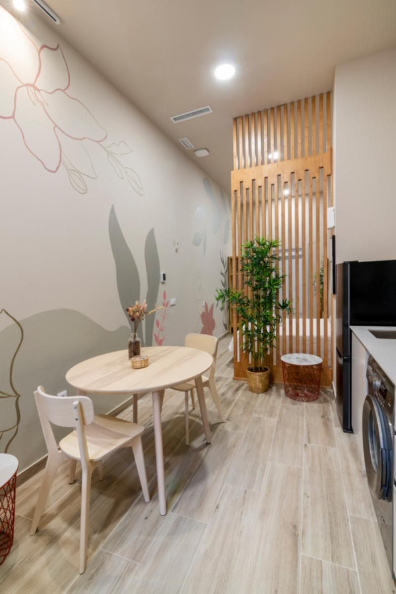 Un coin repas avec une table ronde, des chaises, une plante en pot et un mur orné de motifs floraux abstraits.