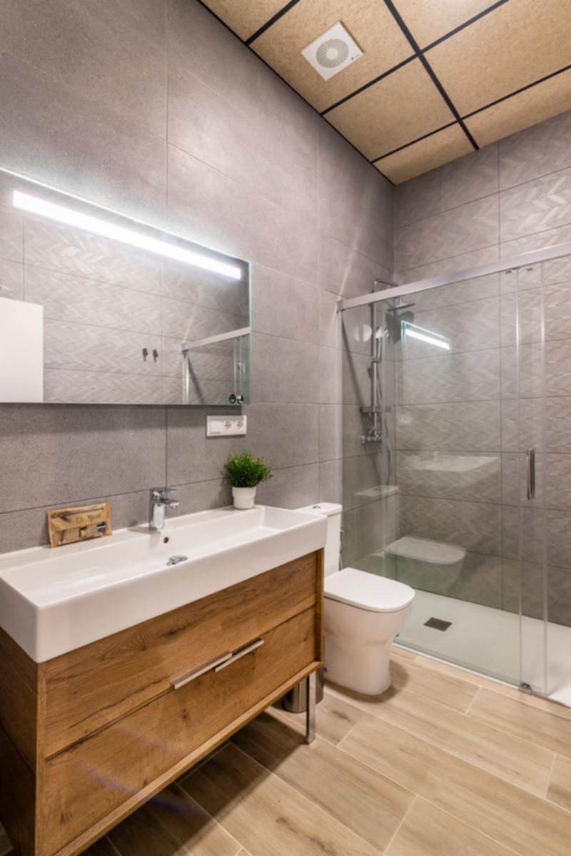 Une salle de bain moderne avec un meuble-lavabo en bois, un lavabo blanc, un miroir, une cabine de douche en verre et des toilettes.