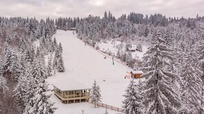 Pista de esquí nevada con una plataforma de madera y una cabaña pequeña.