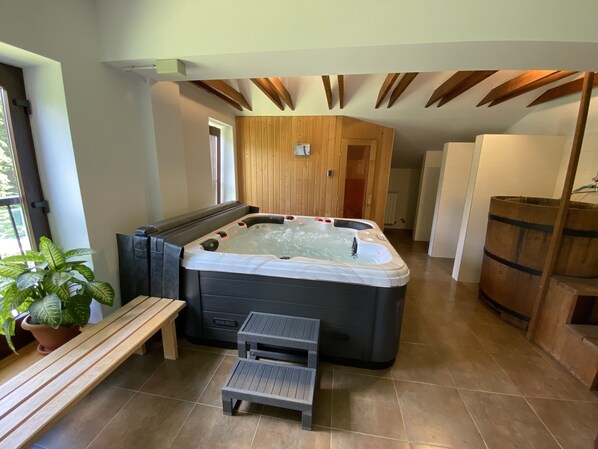 A modern spa room with a hot tub, wooden ceiling beams, a small wooden bench, and a potted plant.