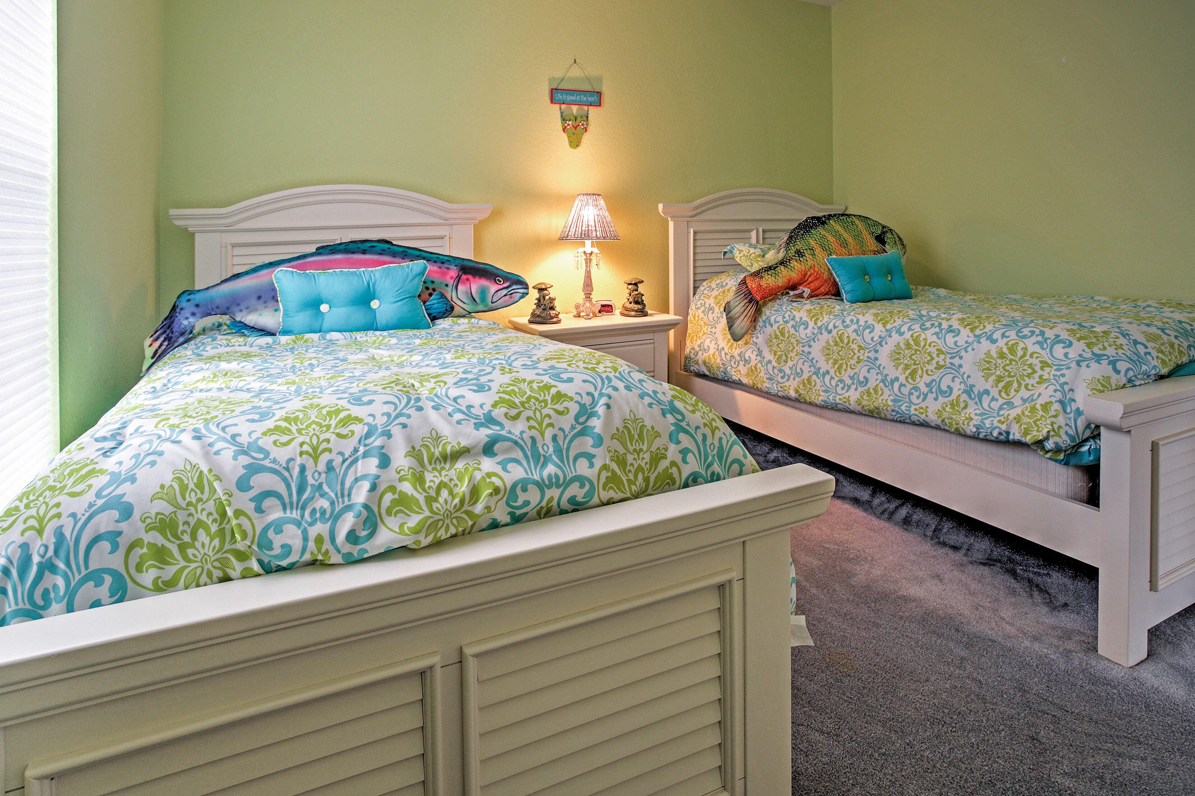 Two twin beds with matching headboards and footboards, a bedside table with a lamp, and a wall hanging above the beds.