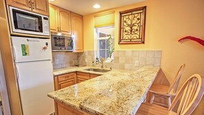 A kitchen with granite countertops, wooden cabinets, a microwave, a refrigerator, a sink, and a chair. - Naples Home w/ Pool, Extended Stays Welcome! (Naples)