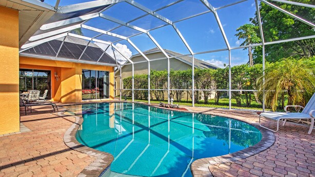 A swimming pool with a glass enclosure, surrounded by a brick patio and outdoor furniture. - Naples Home w/ Pool, Extended Stays Welcome! (Naples)