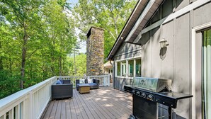 A wooden deck with a stone chimney, outdoor seating, and a barbecue grill. - Outdoor Fireplace + Views Mountain Bearadise (Sapphire)