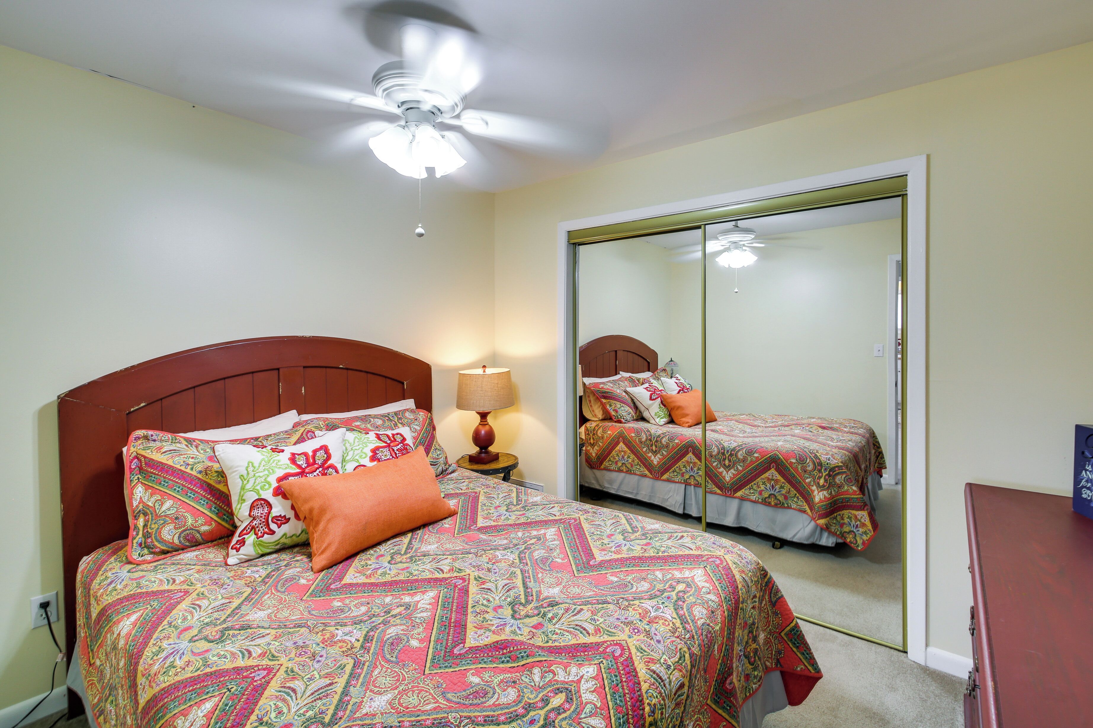 A bedroom with a bed, a nightstand, a lamp, a ceiling fan, and a wardrobe.