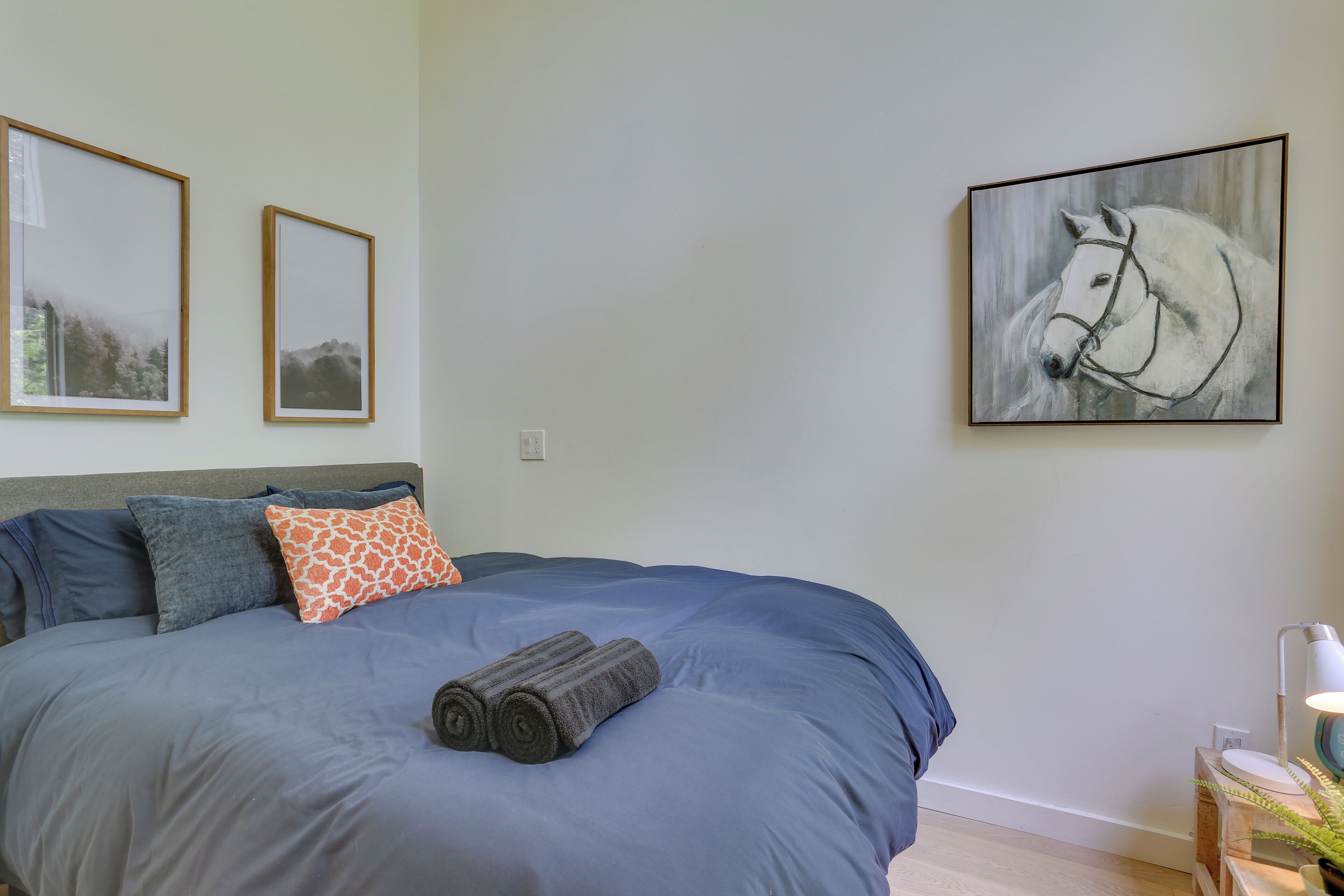 Un dormitorio con una cama grande, dos cuadros en la pared y una lámpara sobre una mesita.