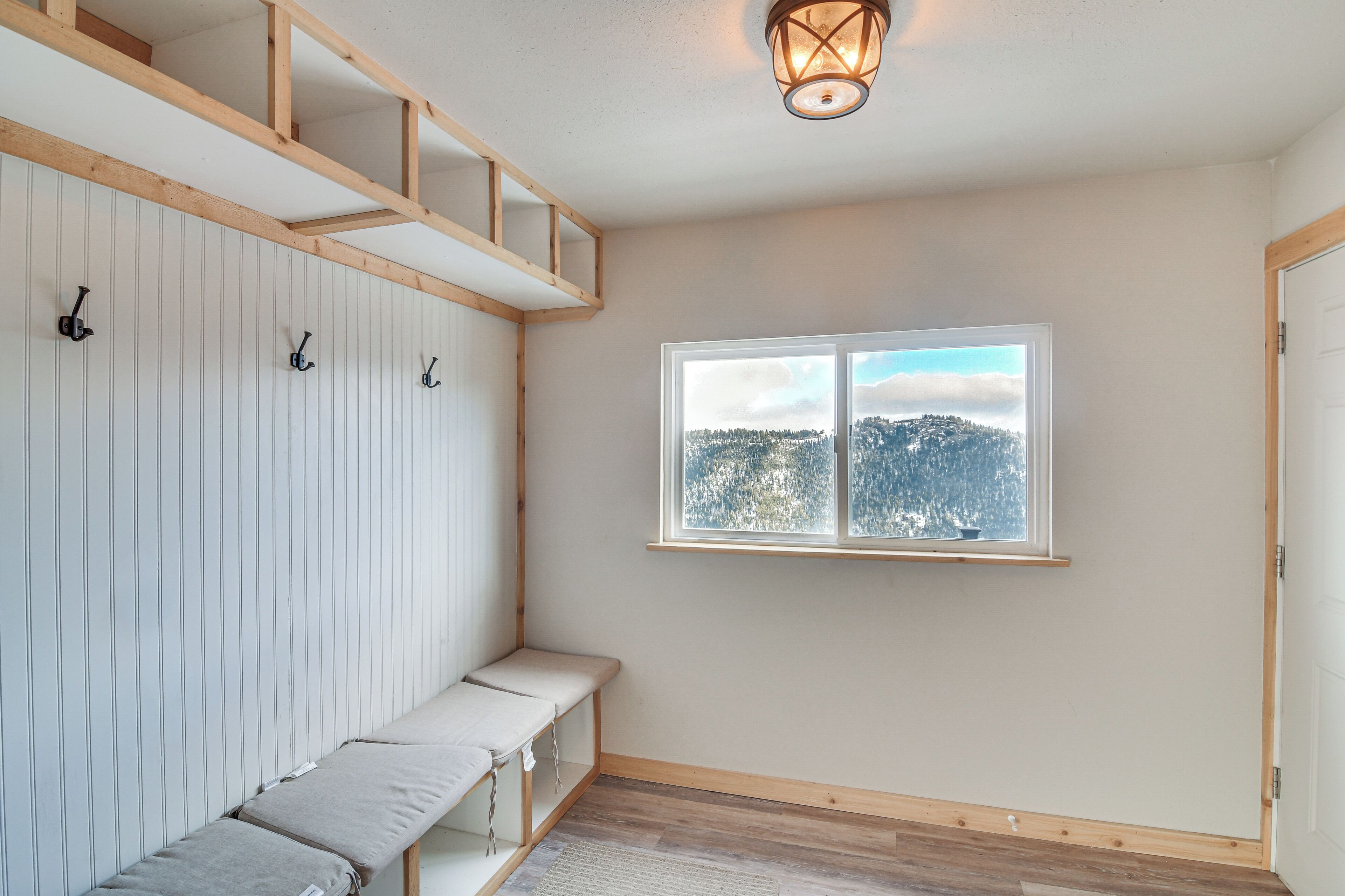 A room with a wooden bench, a window with a view of a snowy landscape, and a wall-mounted light fixture.