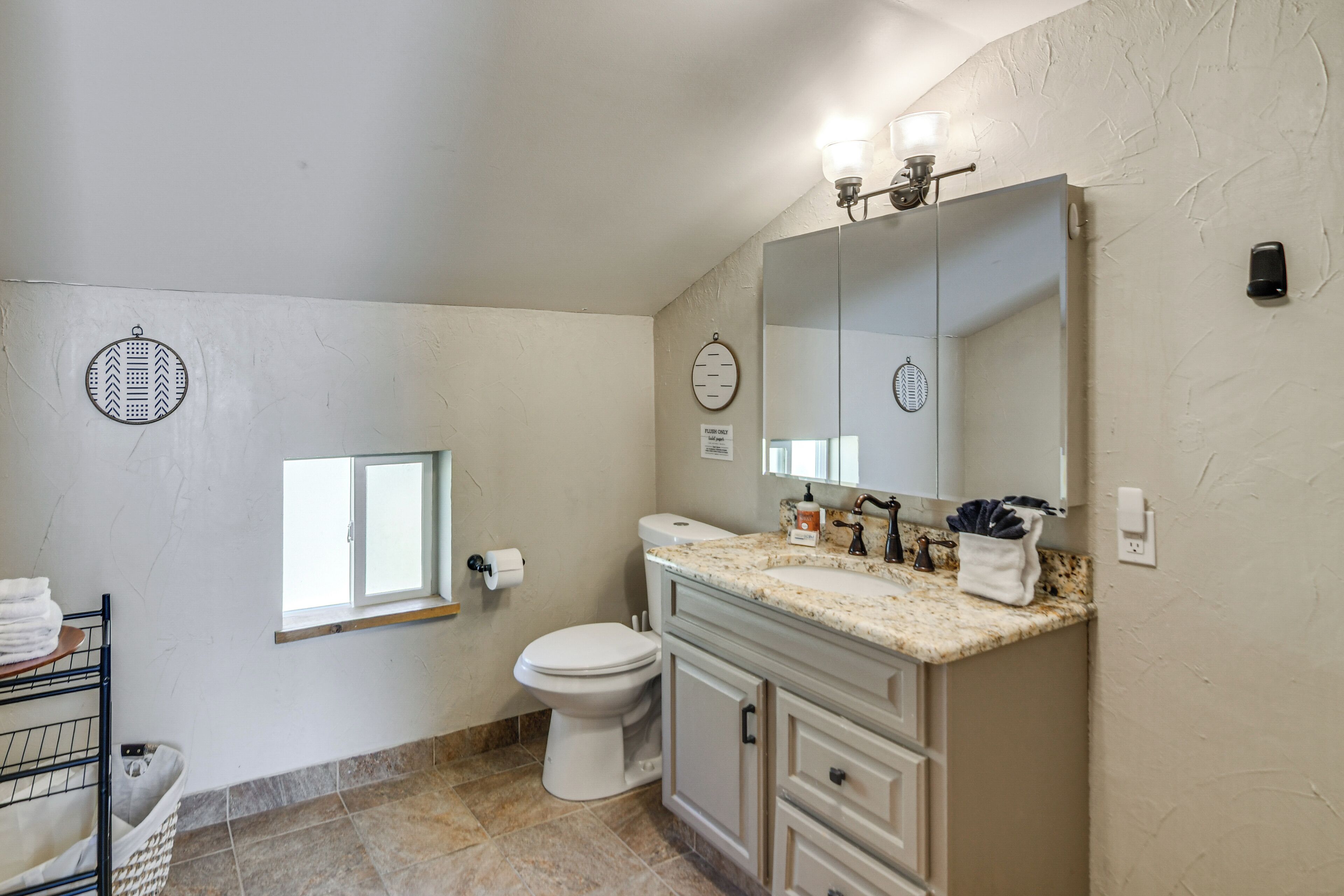 A bathroom with a toilet, sink, and mirror. There is a towel rack and a window.