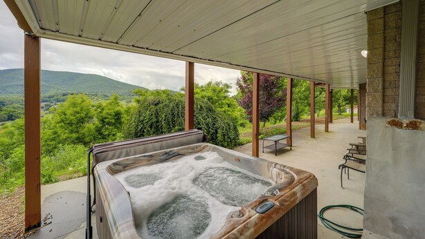 Un bain à remous installé sous une terrasse couverte, avec vue sur des collines verdoyantes.