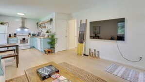 Cocina moderna con armarios blancos, estufa y microondas. Hay una mesa de comedor con sillas y una mesa baja con libros.