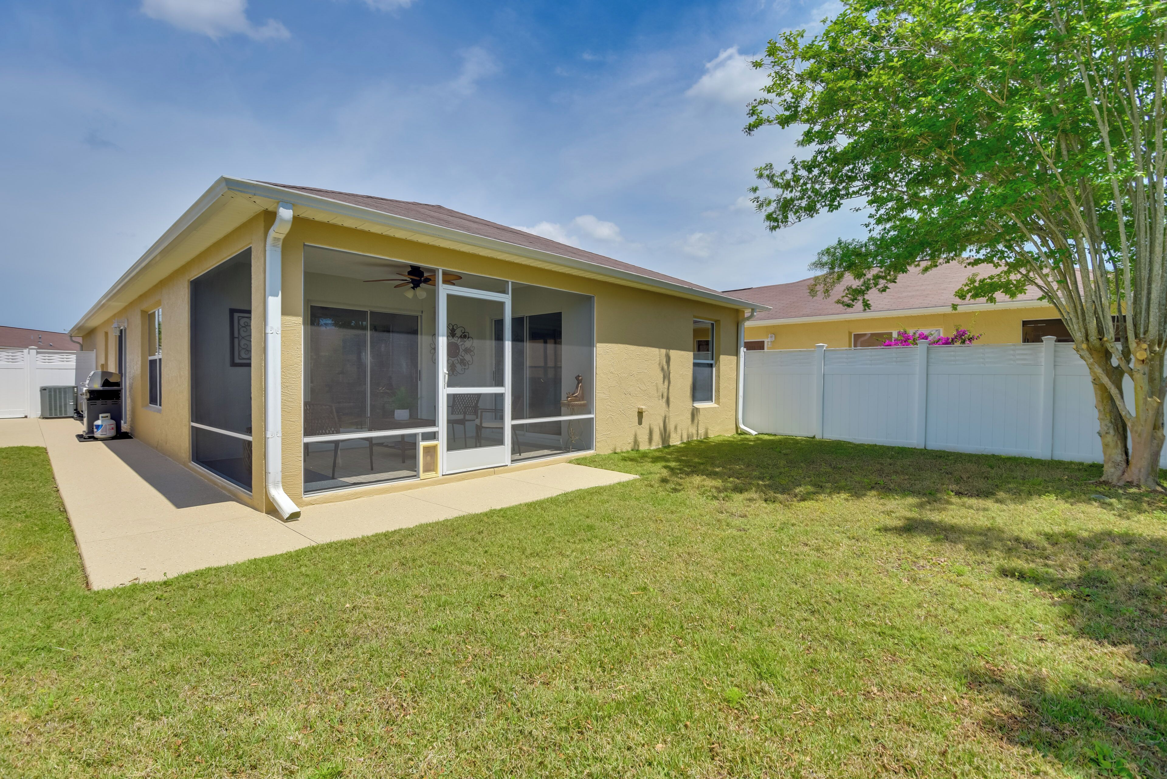 A single-story house with a covered patio, a fenced backyard, and a tree.