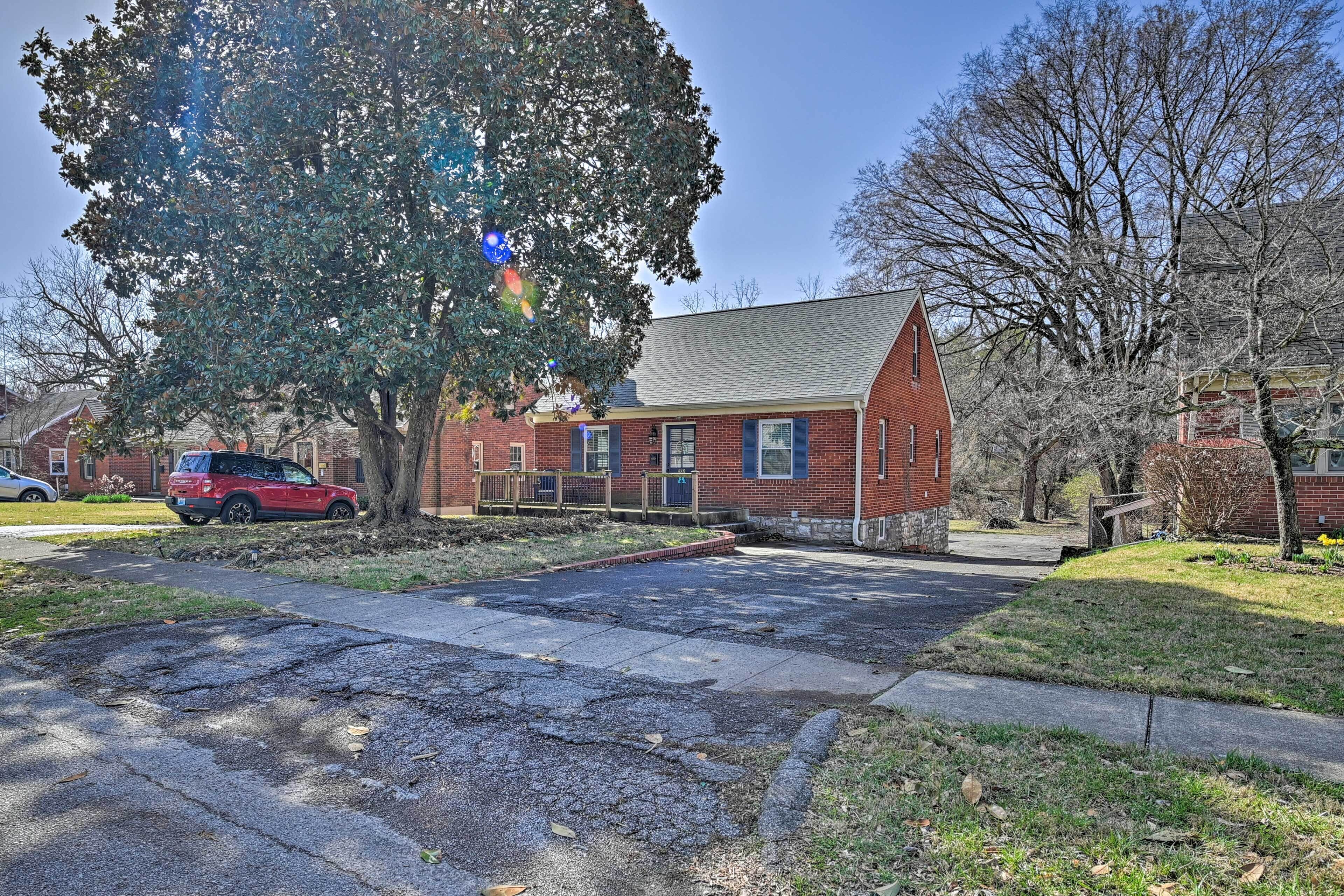 A red brick building with a sloped roof, a front porch, and a tree in front.
