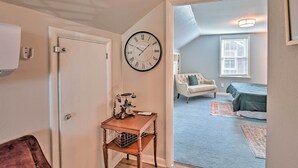 A hallway with a clock, a vintage telephone, and a door leading to a living room with a bed, a chair, and a window. - Spacious Lexington Studio: 2 Miles to Rupp Arena (Lexington)