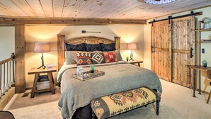 Ein gemütliches Schlafzimmer mit einem großen Bett, einem Holz-Kopfteil, zwei Nachttischen mit Lampen, einer Bank und einer Schiebetür im Bauernhausstil.