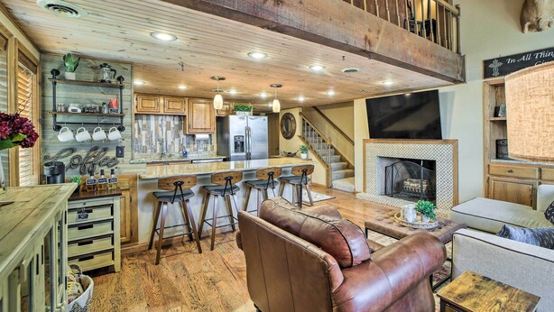 Ein großzügiger Wohnbereich mit hohen Decken, Holzbalken, einem Kamin, einer Bar mit Hockern und einem Ledersofa.