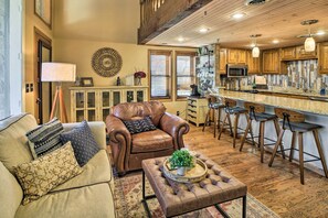 A spacious living area with a leather sofa, a coffee table, and a kitchen with wooden cabinets and a bar. - Balcony w/ Hot Tub: Monkey Island Vacation Rental! (Afton)