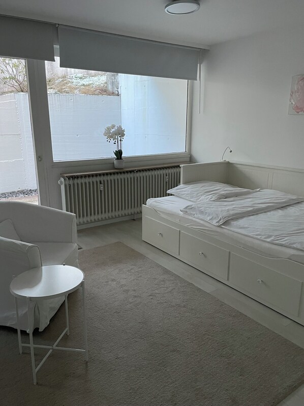 Een slaapkamer met een bed, een stoel, een radiator en een raam met uitzicht.