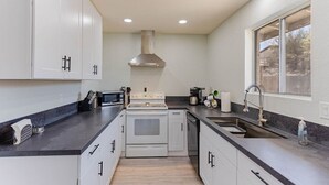 A modern kitchen with white cabinets, a stove, a microwave, and a sink. - Havasu Warbler - Hot Tub, BBQ, Parking, FirePit (Lake Havasu City)