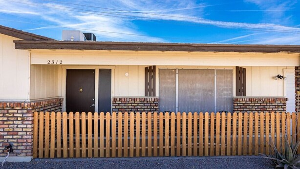 A single-story building with a numbered address, a wooden picket fence, and a gravel driveway. - Havasu Warbler - Hot Tub, BBQ, Parking, FirePit (Lake Havasu City)