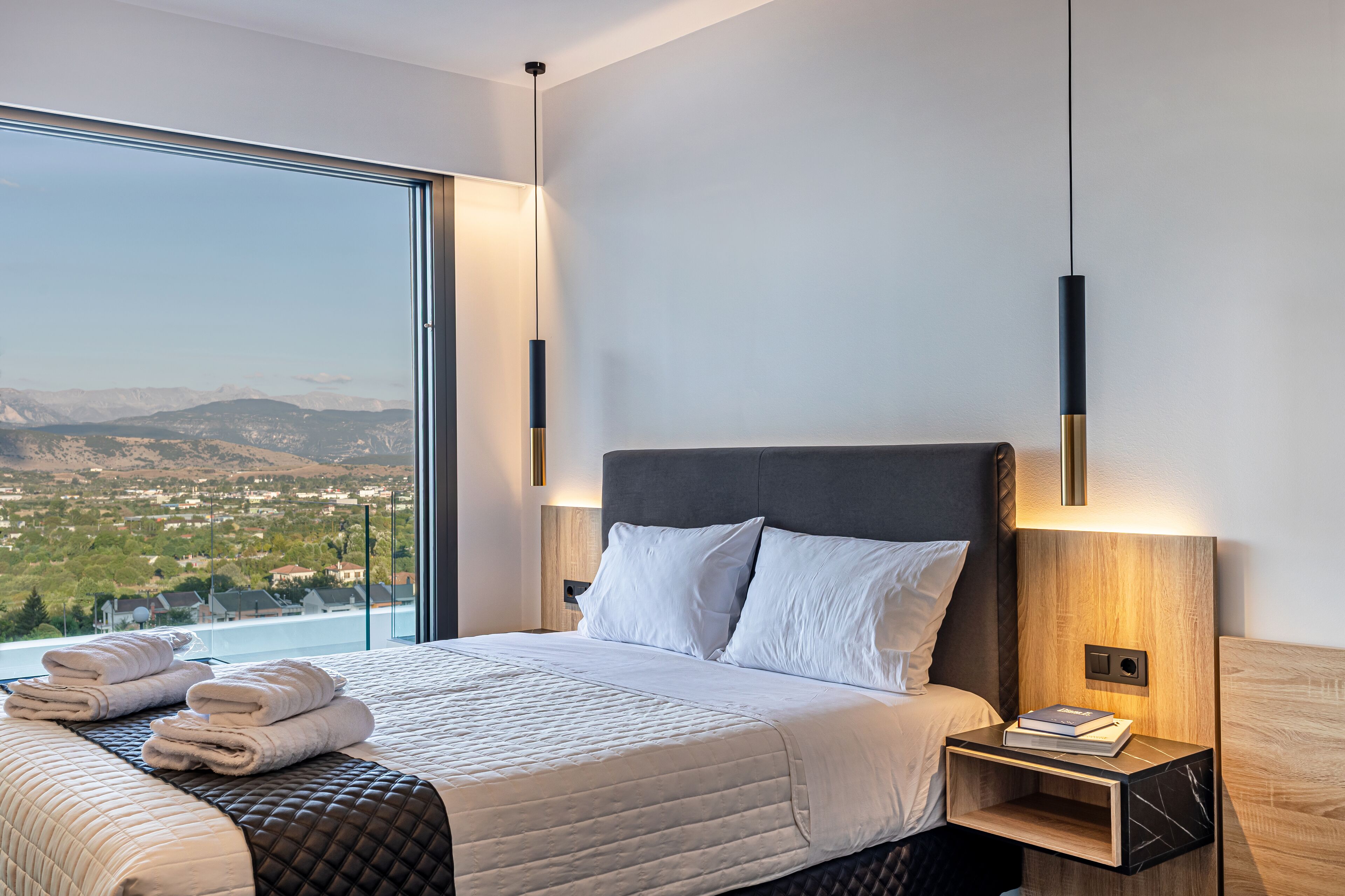 A modern hotel room with a large bed, two bedside tables, and a view of a mountainous landscape.