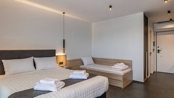 Una habitación de hotel moderna con una cama grande, una cama más pequeña, una mesita de noche, una lámpara y una puerta.
