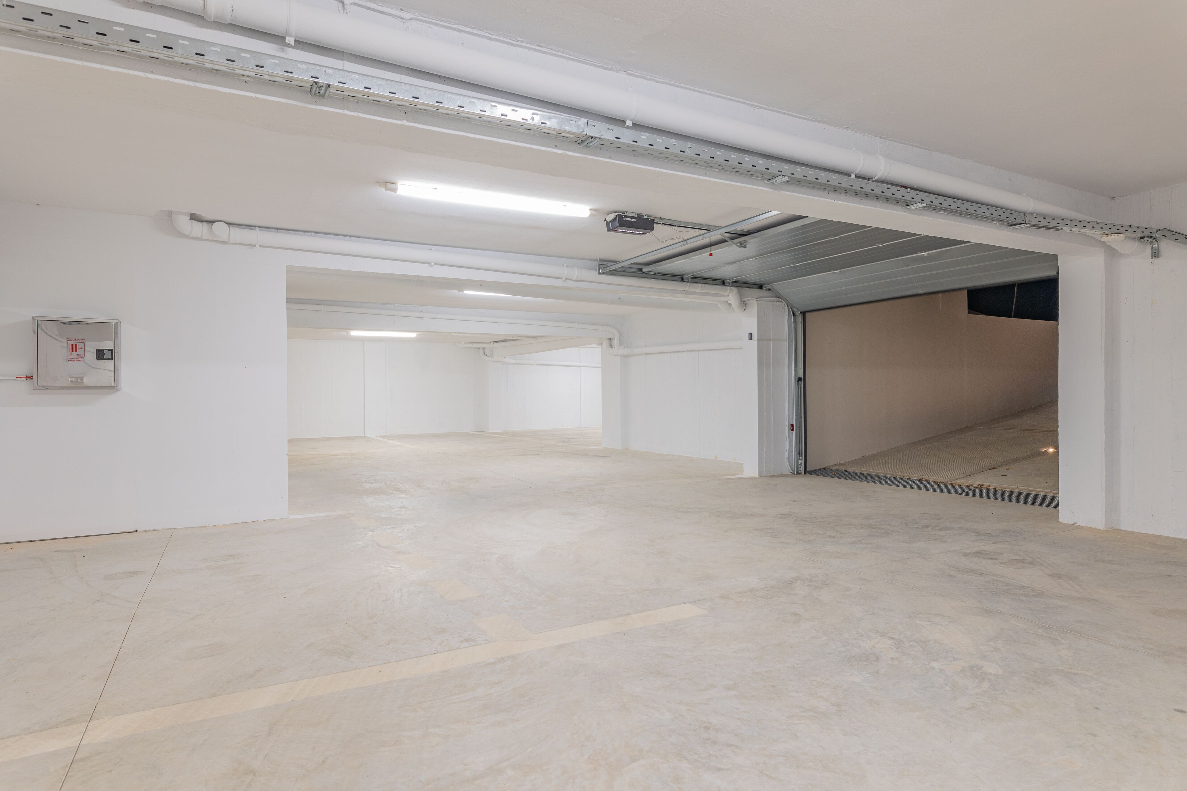 A spacious, empty indoor area with white walls and a concrete floor, featuring a large open door leading to another room.