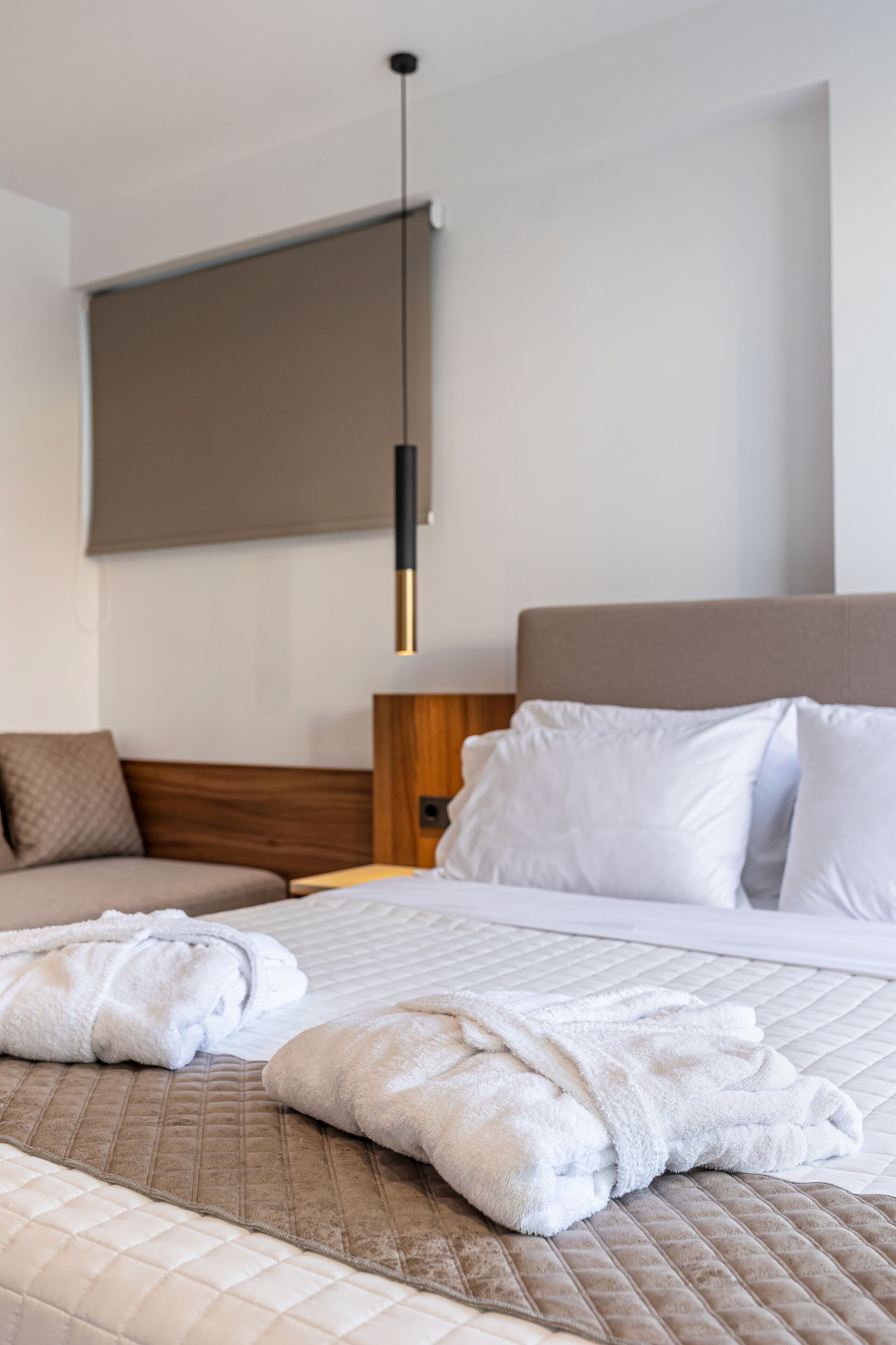 A modern hotel room with a large bed, a wooden headboard, and a hanging light fixture.