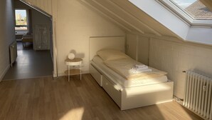 Une petite chambre à coucher moderne avec un plafond en pente et un puits de lumière, un lit simple, une table de chevet et un radiateur.