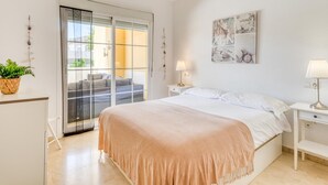 Een slaapkamer met een bed, nachtkastje, lamp, kunstwerk aan de muur en een schuifdeur naar een terras.