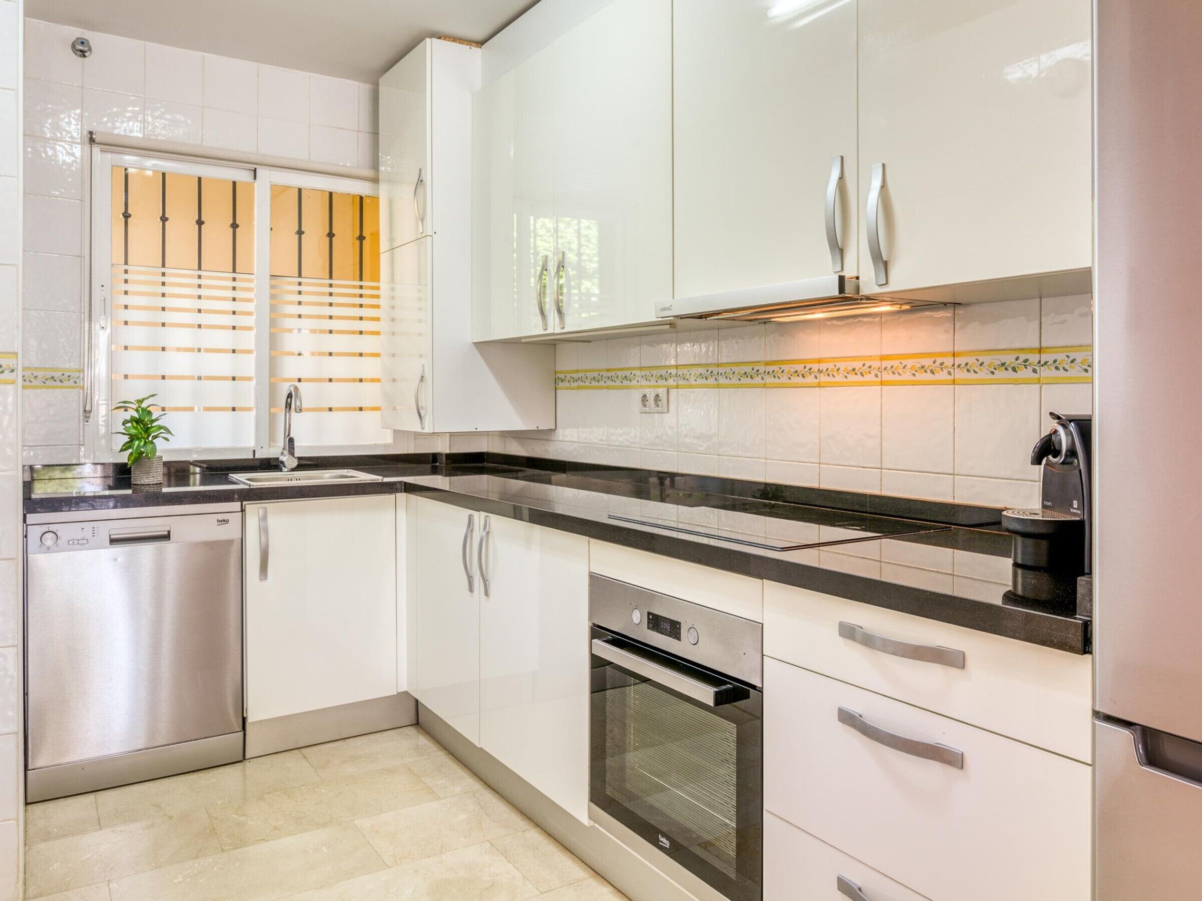 A modern kitchen with white cabinets, a stainless steel dishwasher, an oven, and a coffee machine.