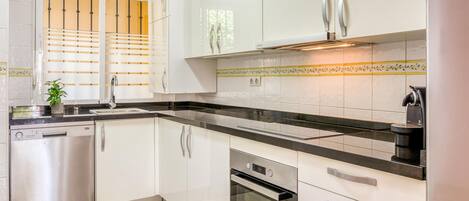 A modern kitchen with white cabinets, a stainless steel dishwasher, an oven, and a coffee machine.