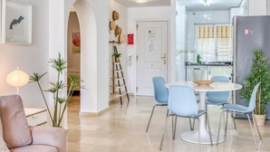 Een moderne woonkamer met een bank, een eettafel met stoelen, een keuken met een koelkast, en een trap naar een andere verdieping.