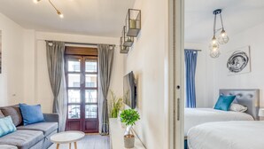 Une chambre d’hôtel moderne comprenant un canapé, une petite table, une table de chevet avec une plante, un lit avec une tête de lit et un téléviseur fixé au mur.