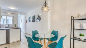 Une cuisine moderne dotée d’un îlot central, d’un coin repas avec des chaises de couleur turquoise et une table en verre, et d’un mur orné de tableaux encadrés.