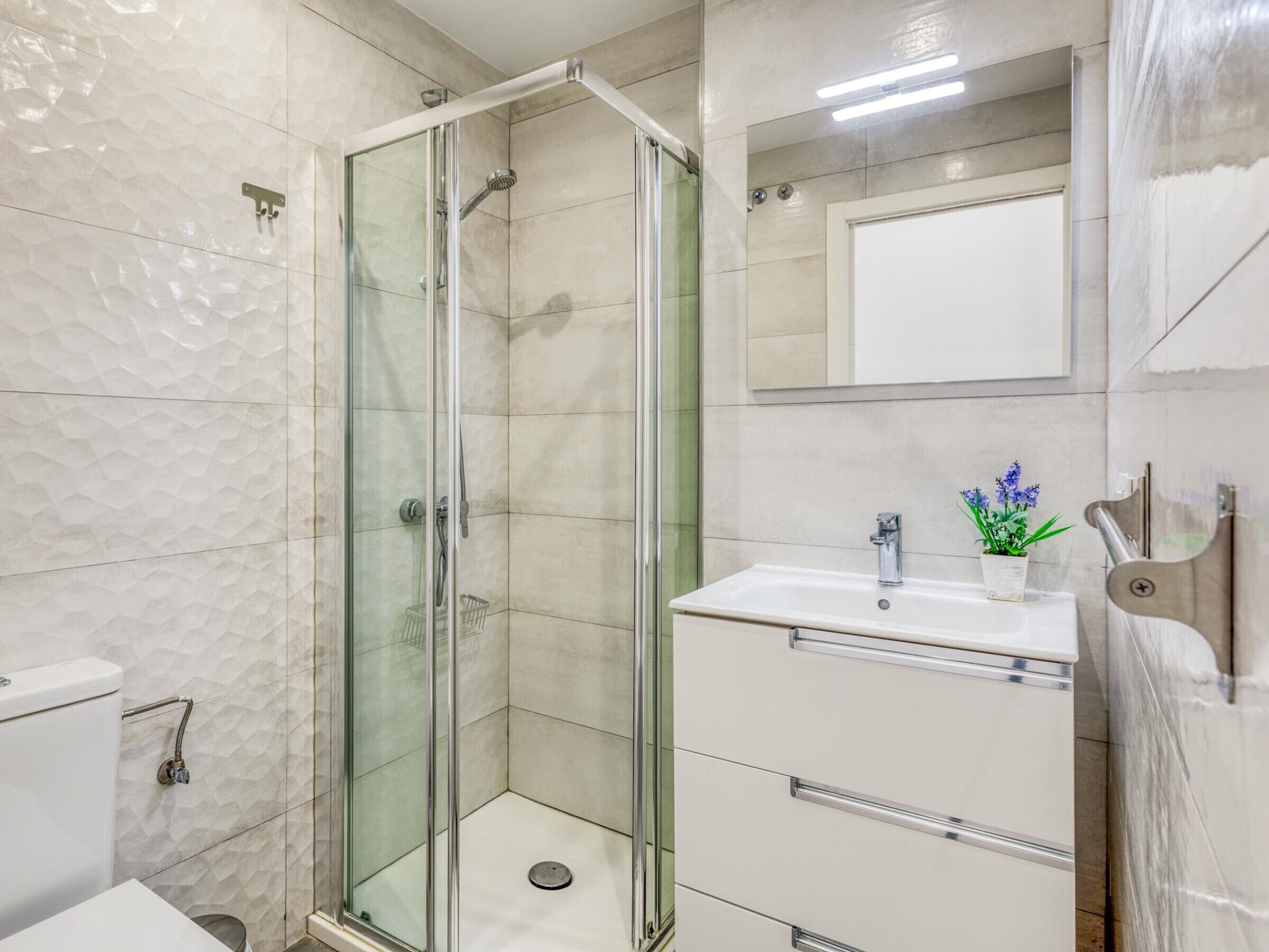 Un bagno moderno con doccia vetrata, lavandino bianco con specchio sopra e il water a sinistra.